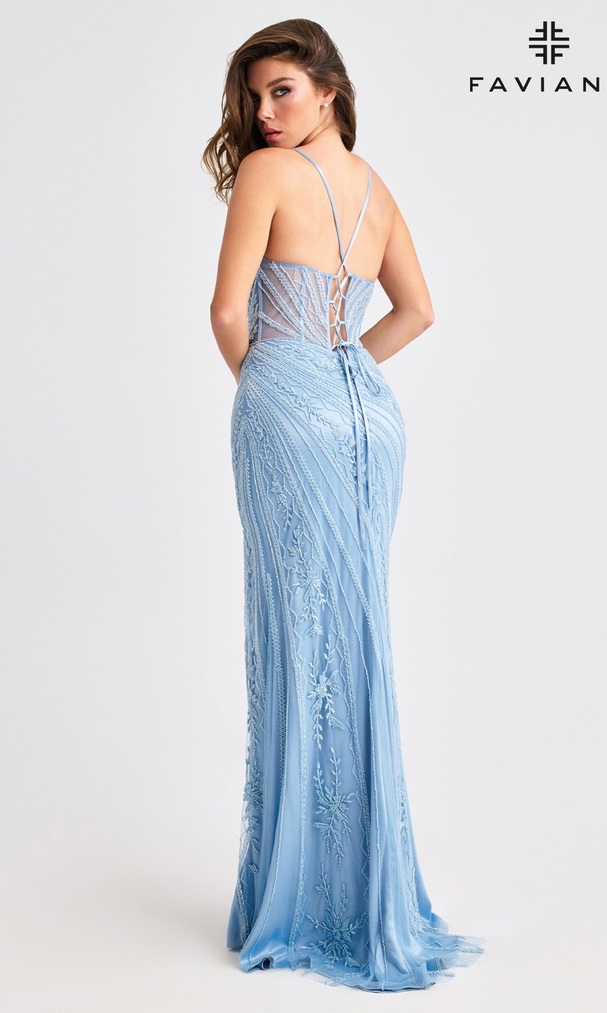 A woman in the Faviana 11409 long prom dress, featuring light blue lace, thin straps, a lace-up back, intricate embroidery, a fitted silhouette, and a sheer corset bodice, stands with the FAVIAN logo visible.